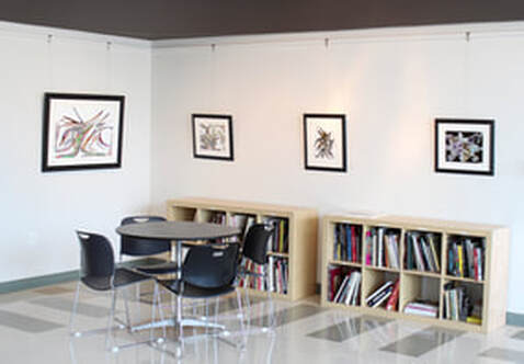 The Bruce H. Lien Cultural Cafe Gallery with bookshelves, a table and chairs, and paintings on the wall.