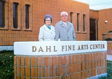 Arndt Dahl and his wife Lillie Dahl stand in front of the sign for the Dahl Fine Arts Center.
