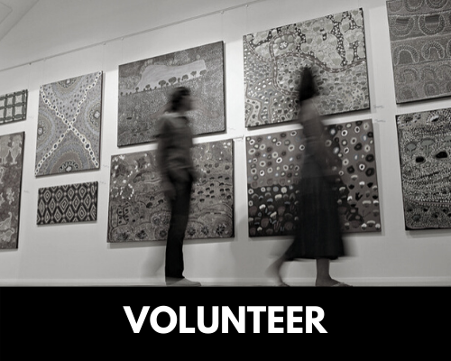 A button for the volunteer page. A blurred, black and white image of a couple walking by paintings on a wall.
