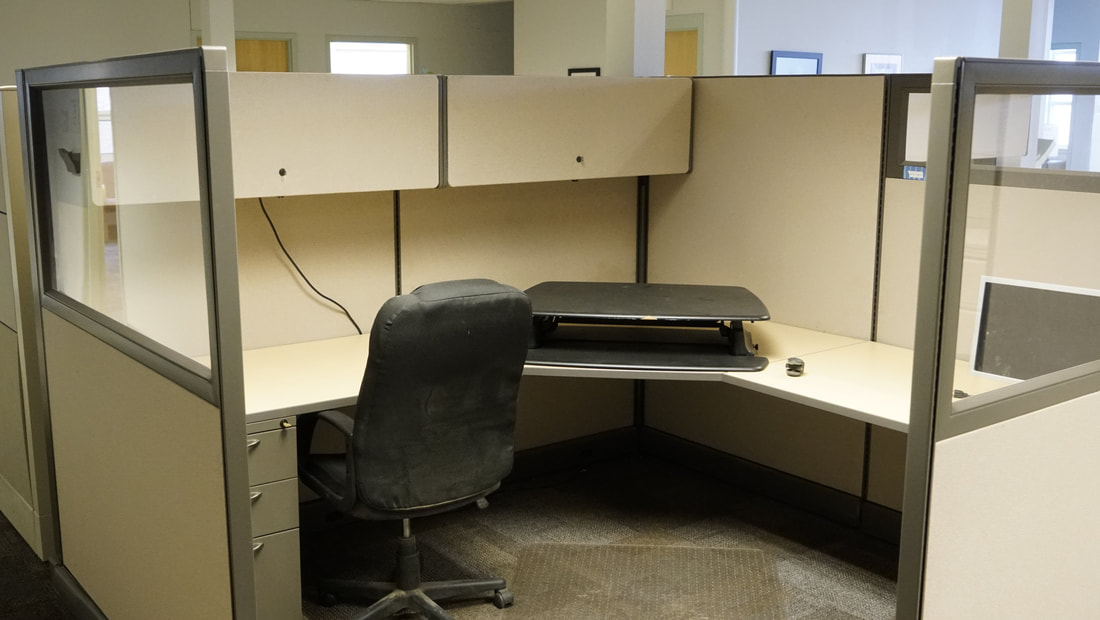 A desk space with an office chair and computer riser. There are 2 cabinets above and 3 drawers below.