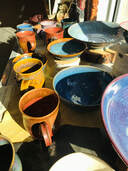 A selection of handmade mugs and bowls in a variety of colors for sale.